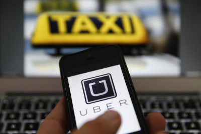 An illustration picture shows the logo of car-sharing service app Uber on a smartphone next to the picture of an official German taxi sign