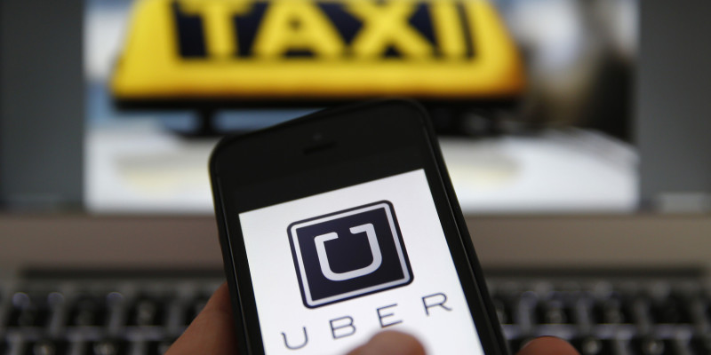 An illustration picture shows the logo of car-sharing service app Uber on a smartphone next to the picture of an official German taxi sign